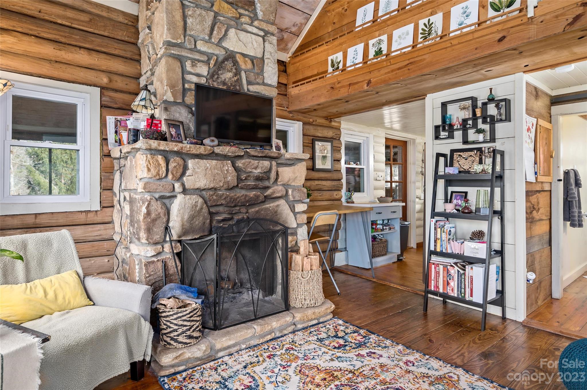 Log home living room with a large stone fireplace, exposed timber walls, and a colorful area rug.