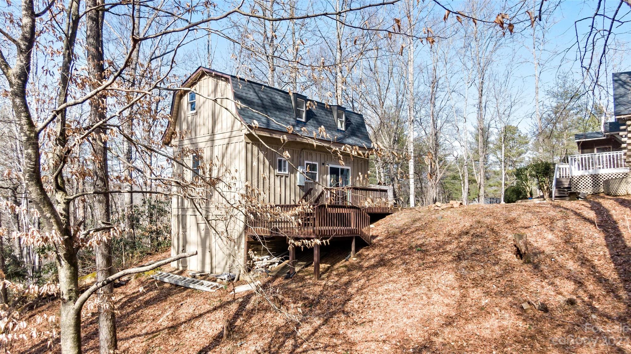 Wood-sided house with a raised deck on a steep, wooded lot.