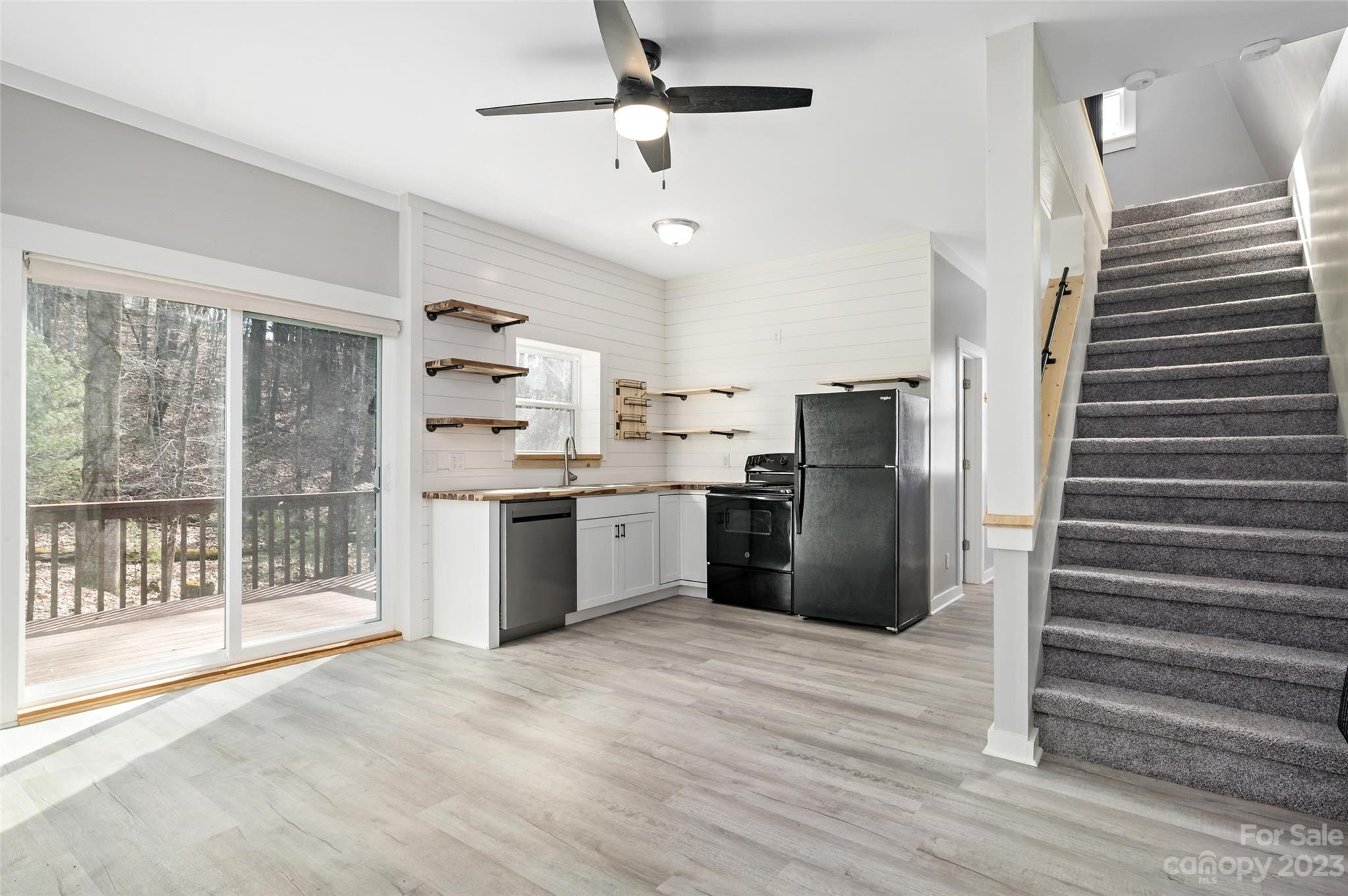 Kitchen with white shiplap walls, wood countertops, black appliances, deck access, and carpeted stairs.