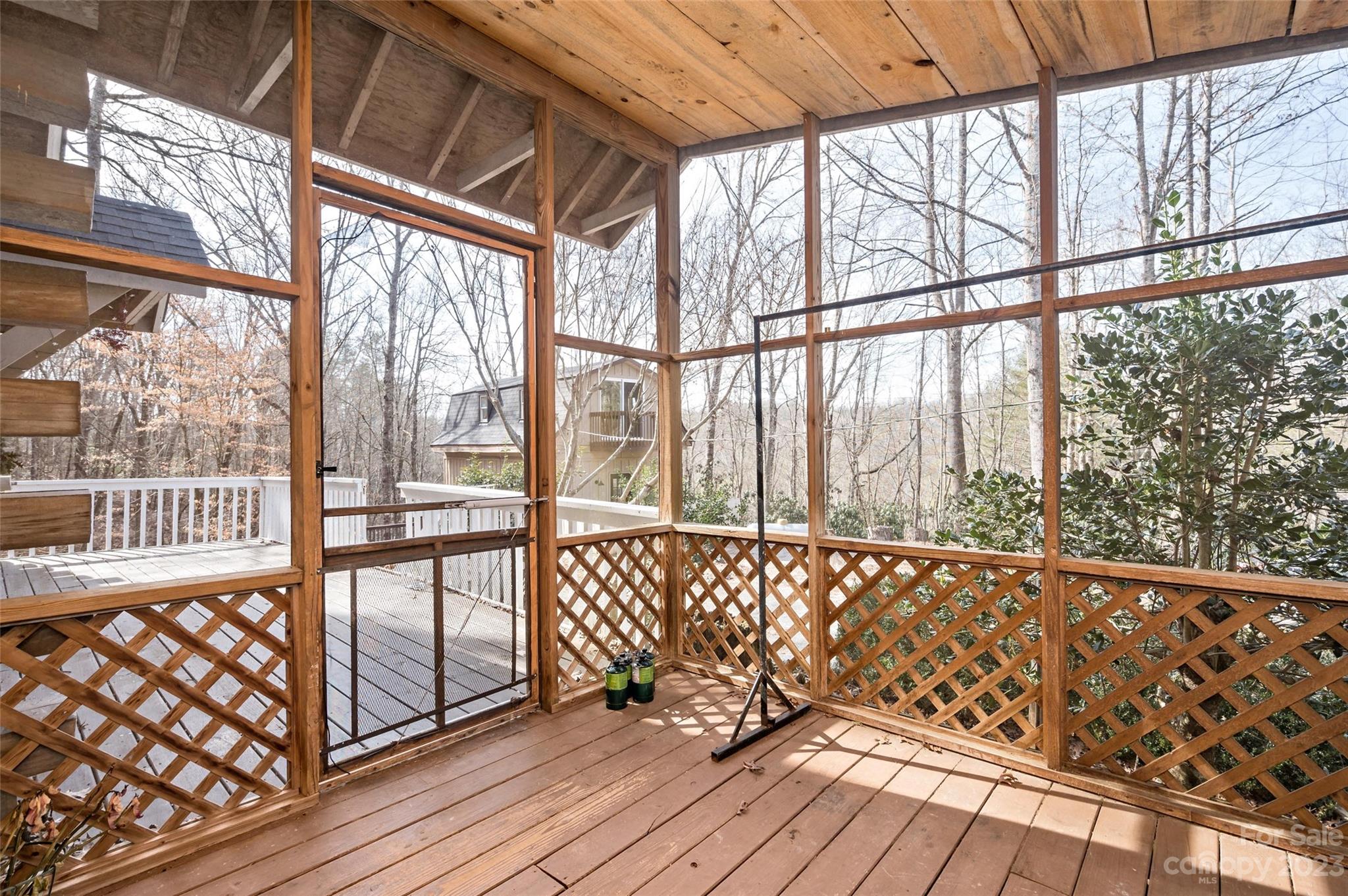 Covered wooden deck with lattice railings, a metal gate, and a view of leafless trees.