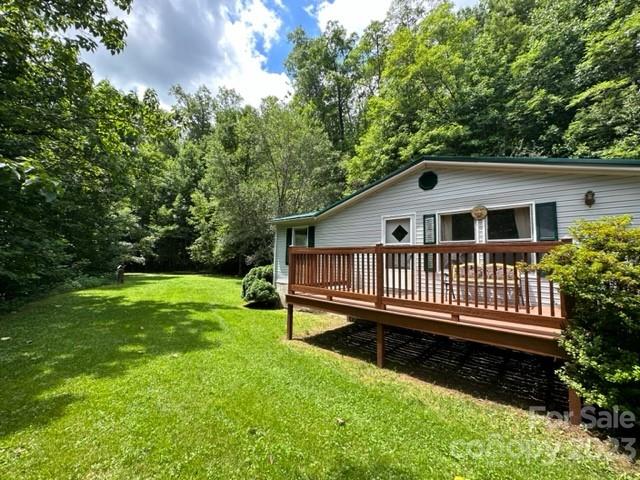 Wooded home exterior with a raised wooden deck overlooking a broad green lawn.