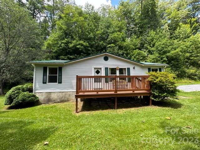 Single-story white home with a raised wooden deck, surrounded by trees.