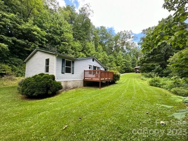 White single-story home with a wooden deck beside a broad lawn and wooded surroundings.