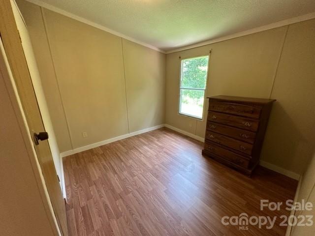 Mostly empty bedroom with laminate flooring, a window, and a dark wooden chest of drawers.