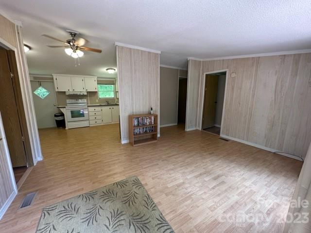 Living room with light wood-look flooring, pale paneled walls, and an open white kitchen.