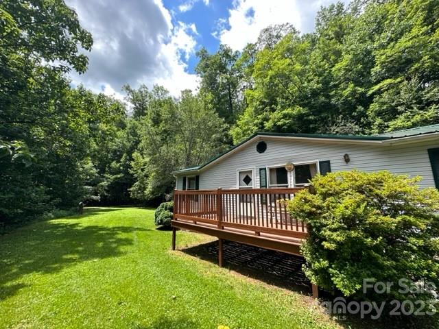 Single-story home with a raised wooden deck overlooking a sunny lawn and wooded surroundings.