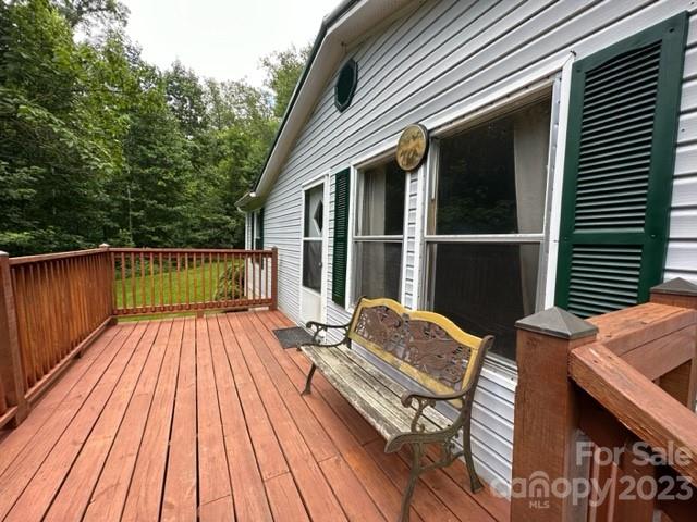 Wooden deck beside a white-sided home, with green shutters and a weathered bench.