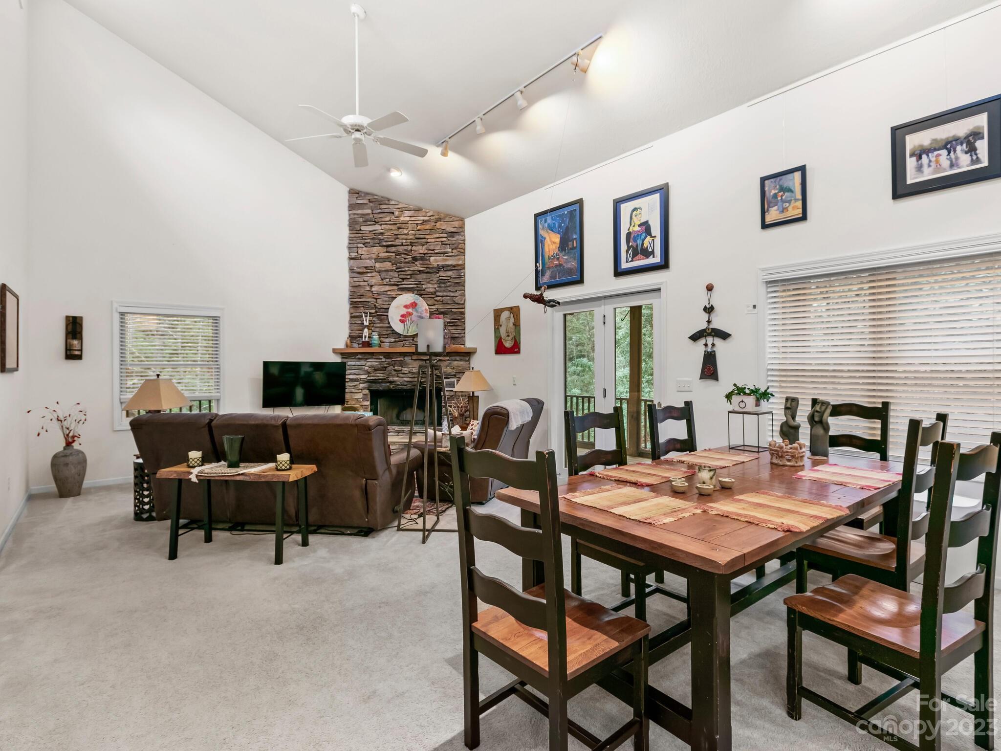 Open living and dining room with a vaulted ceiling, stone fireplace, and large wooden dining table.