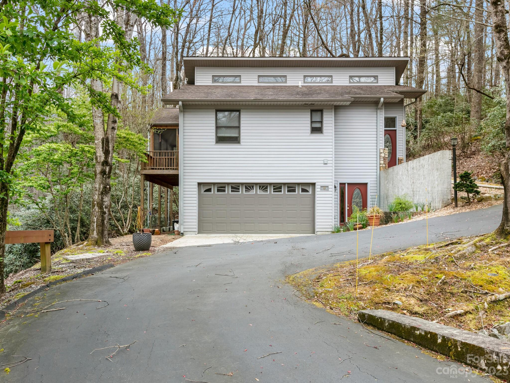 White-sided two-story house with a double garage, red doors, and a covered balcony amid trees.