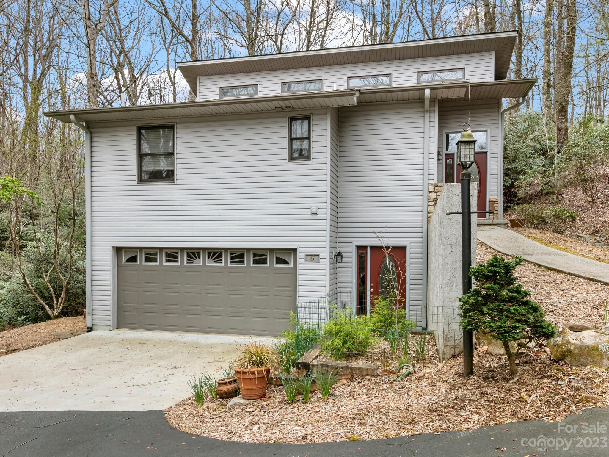 Two-story gray-sided home with a large garage, red doors, and landscaped grounds among leafless trees.