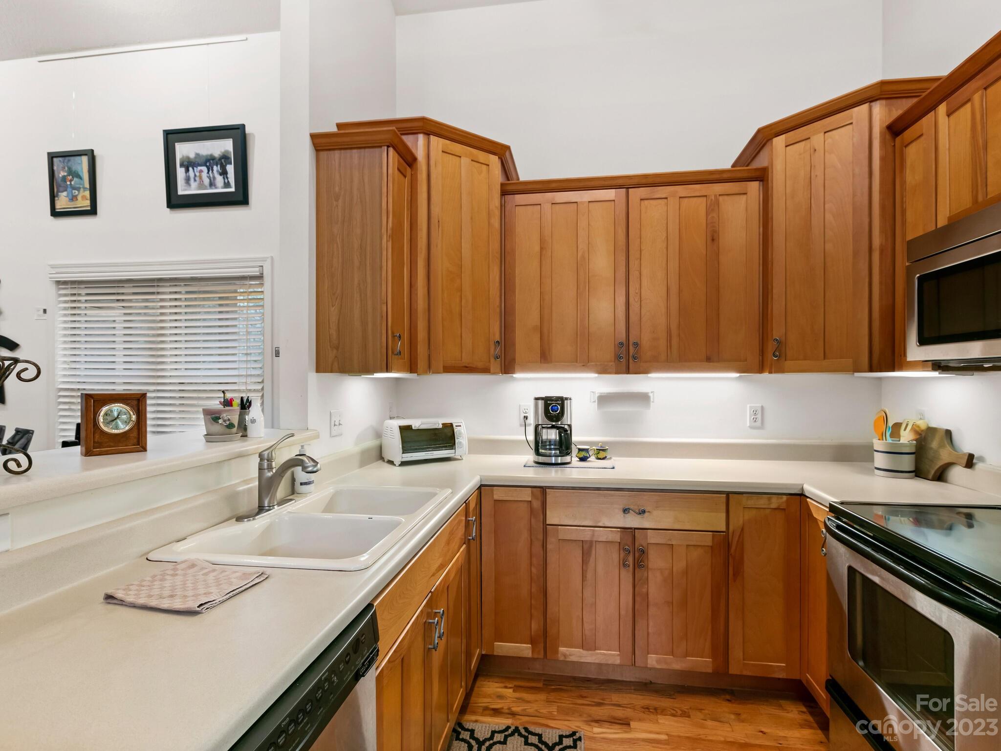 Kitchen with warm wood cabinetry, light countertops, a double-basin sink, and stainless steel appliances.
