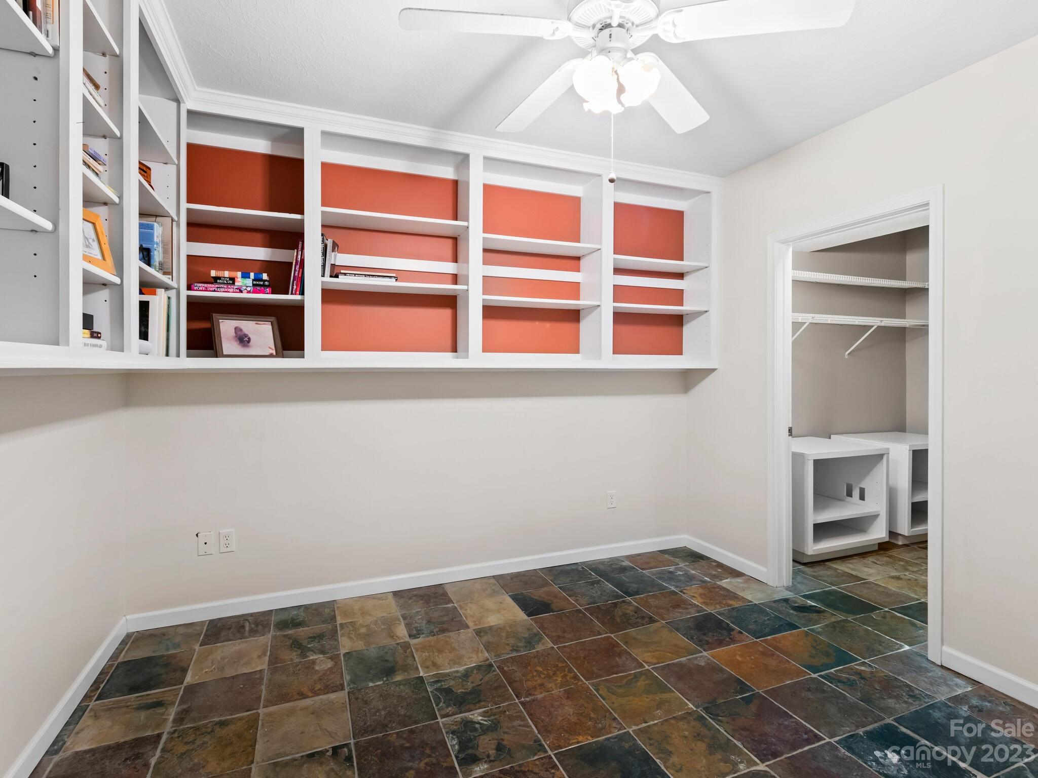 Office with coral-backed built-in shelves, a ceiling fan, multicolored tile floor, and adjoining closet.