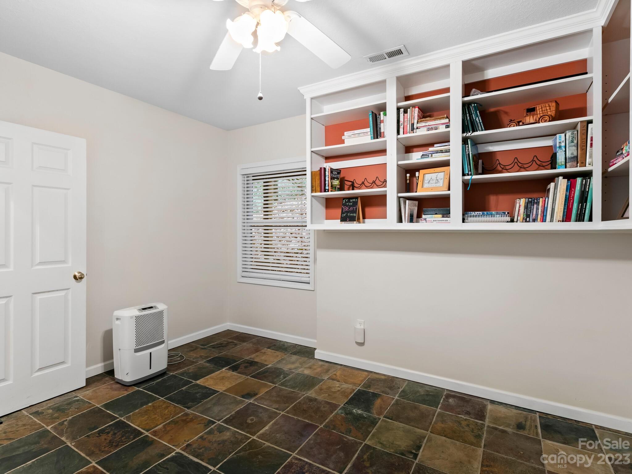 Room with built-in bookshelves, terracotta-colored backing, and multicolored slate tile flooring.
