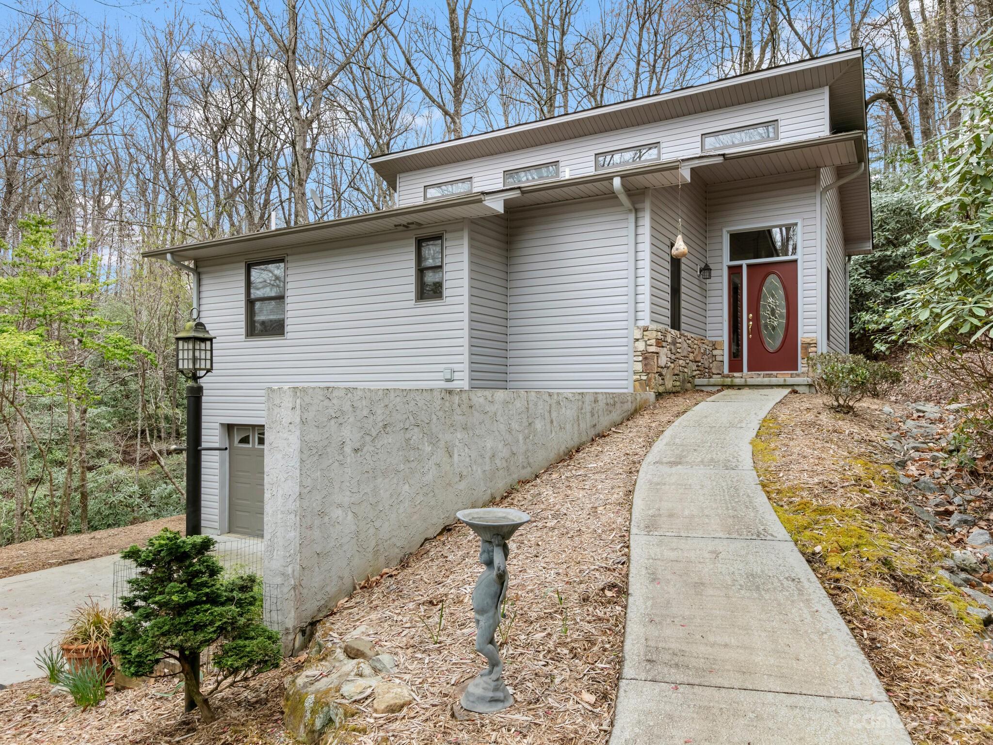 Modern gray-sided home with a red front door, curved walkway, and wooded sloping yard.