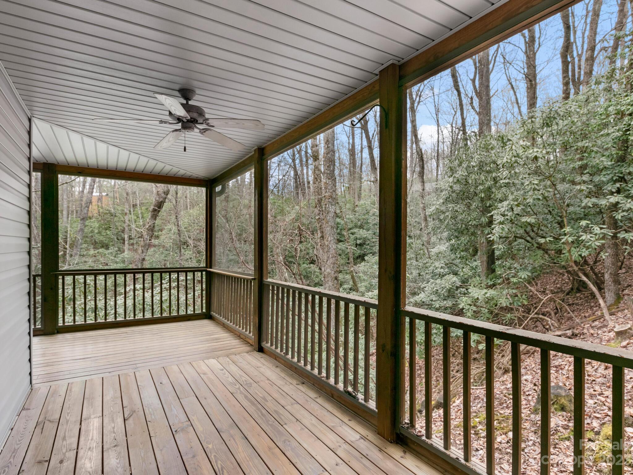 Covered wooden porch overlooking a wooded hillside, with a ceiling fan and dark railings.