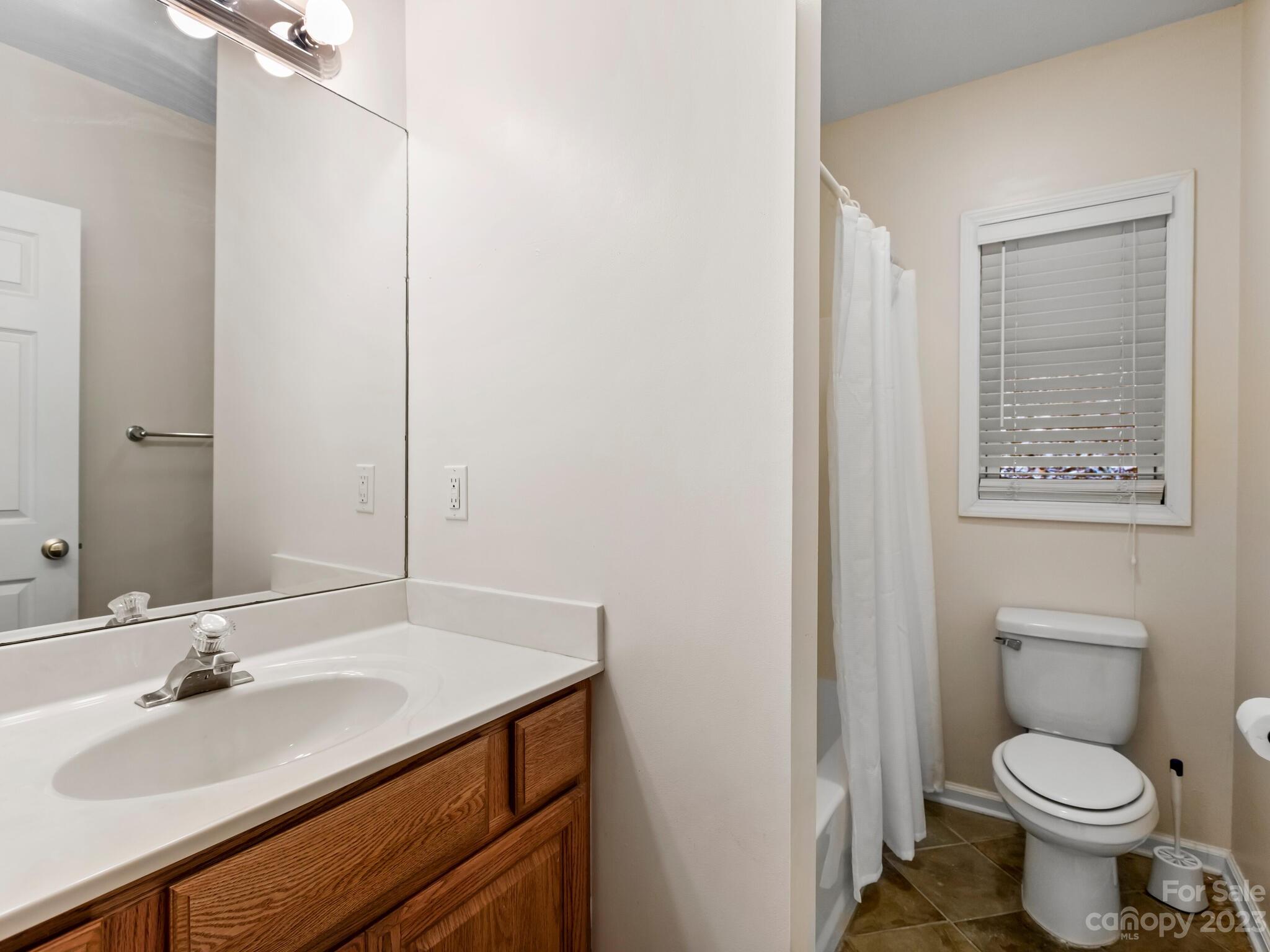Bathroom with a wood vanity, large mirror, and separate toilet and curtained tub-shower area.