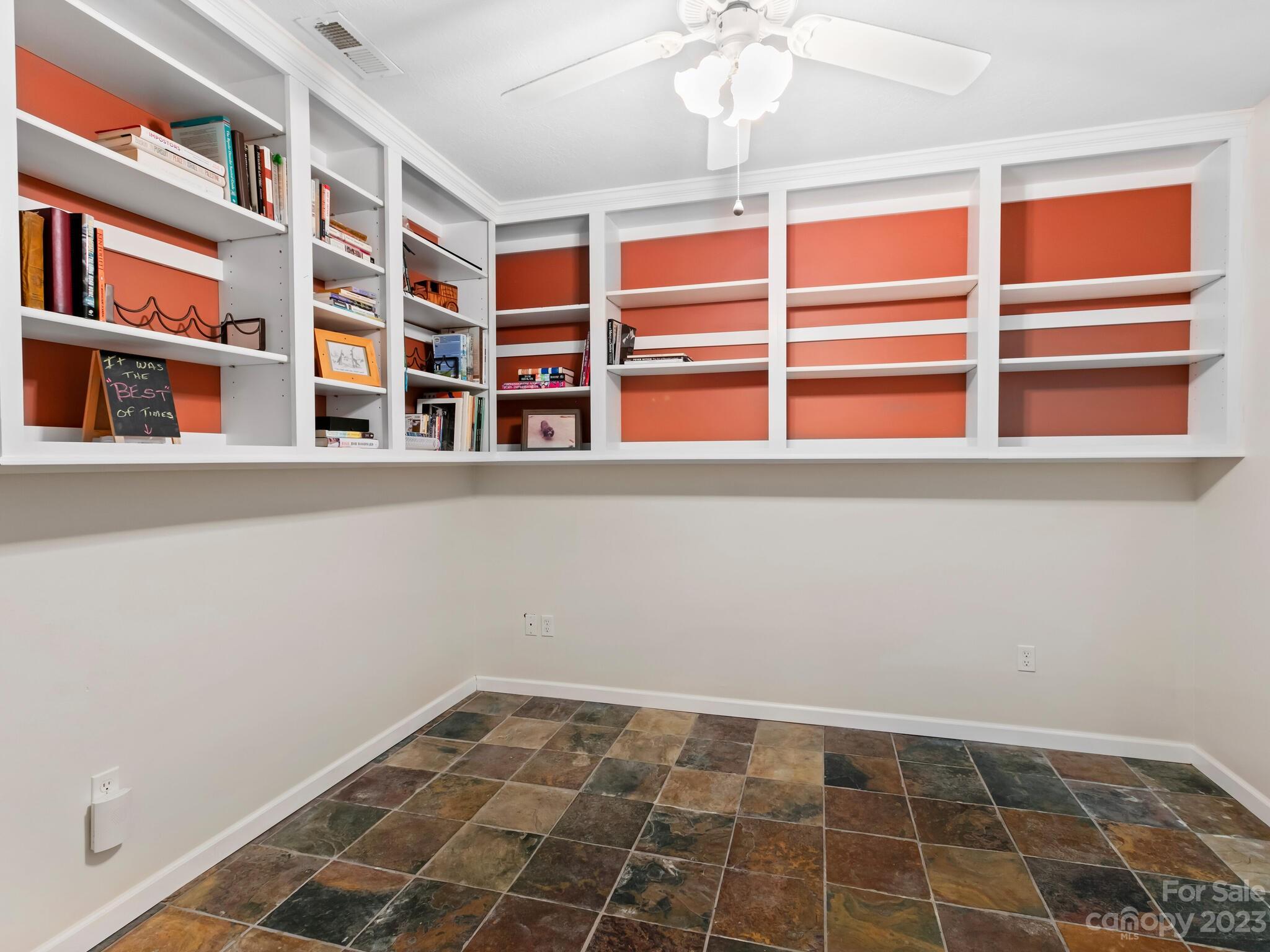 Room with white built-in bookshelves, coral-orange back walls, and multicolored tile flooring.