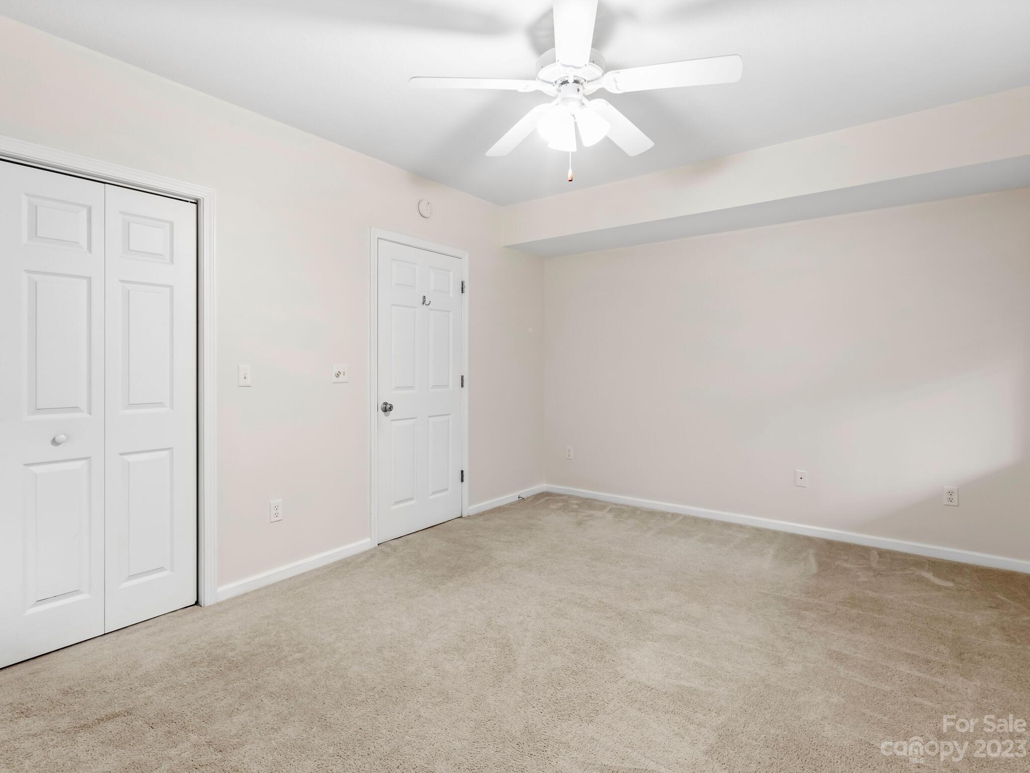 Empty carpeted bedroom with white closet doors and a ceiling fan.