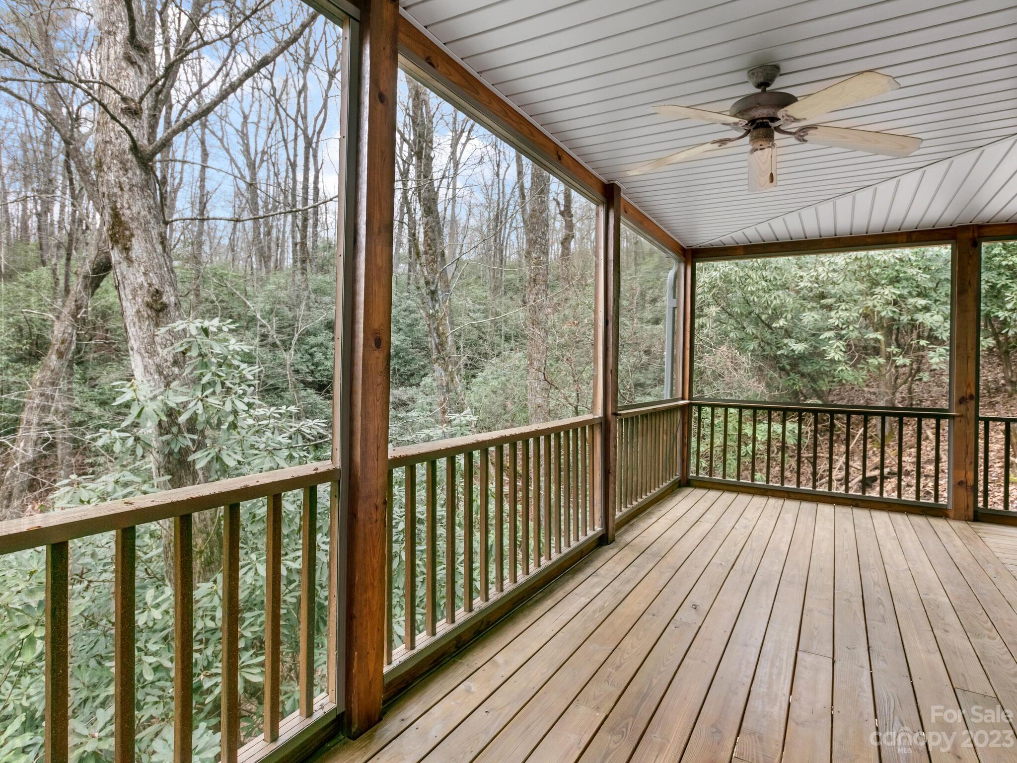 Screened wooden porch overlooking wooded greenery, with a ceiling fan and plank flooring.
