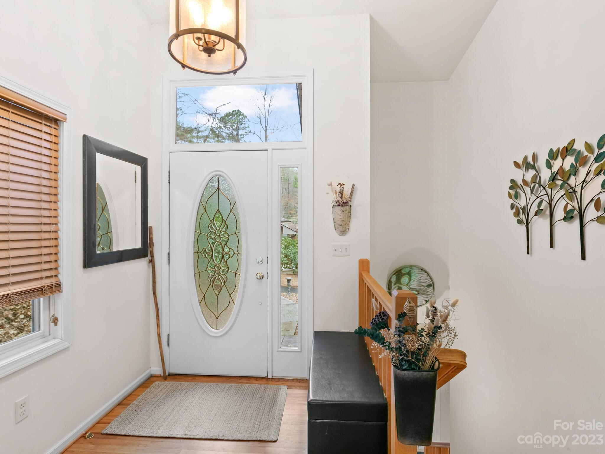 Entry foyer with an ornate oval glass front door, transom window, and wood stair railing.