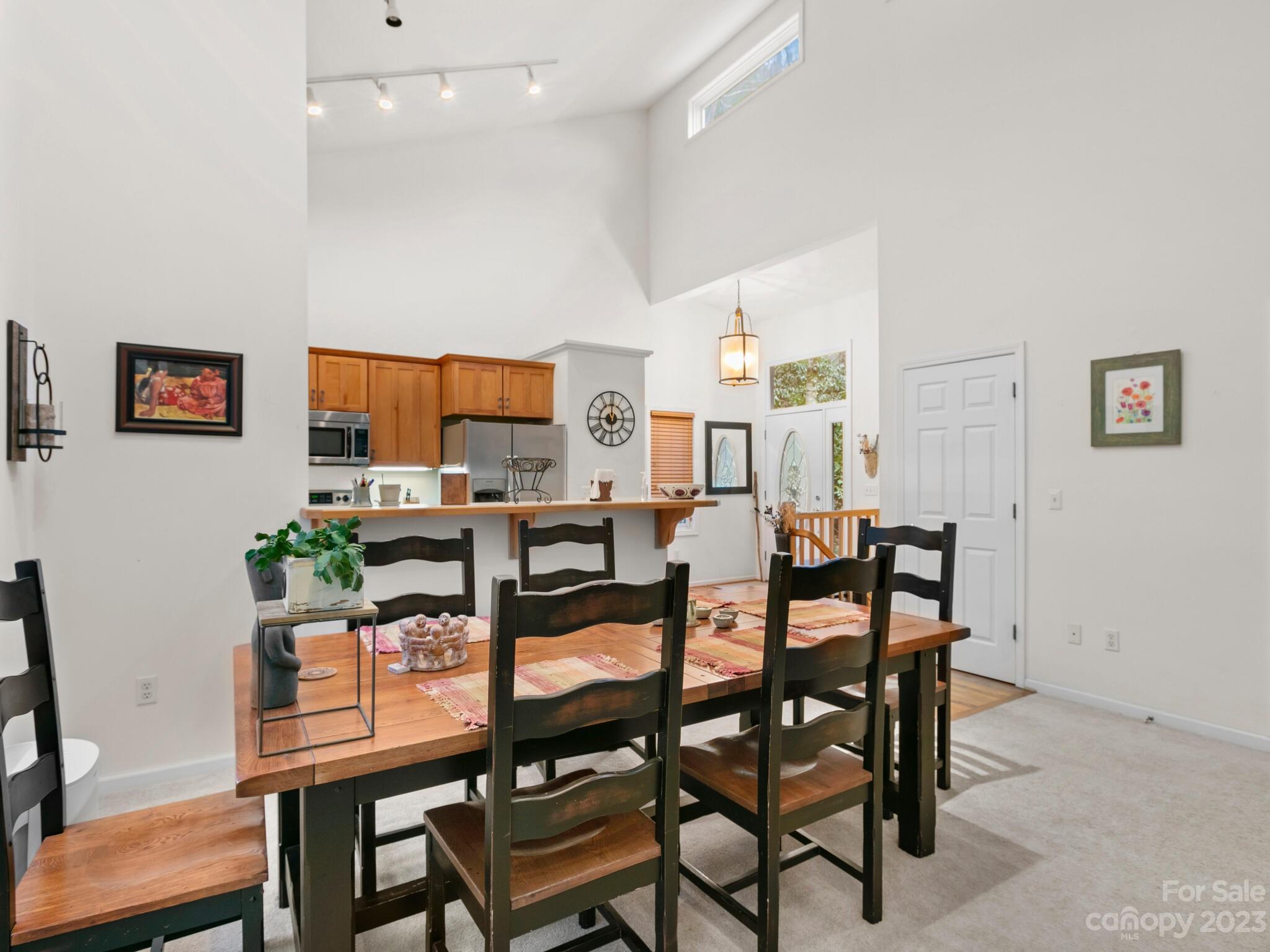 Dining area with a long wooden table and dark chairs beside an open kitchen with wood cabinets.