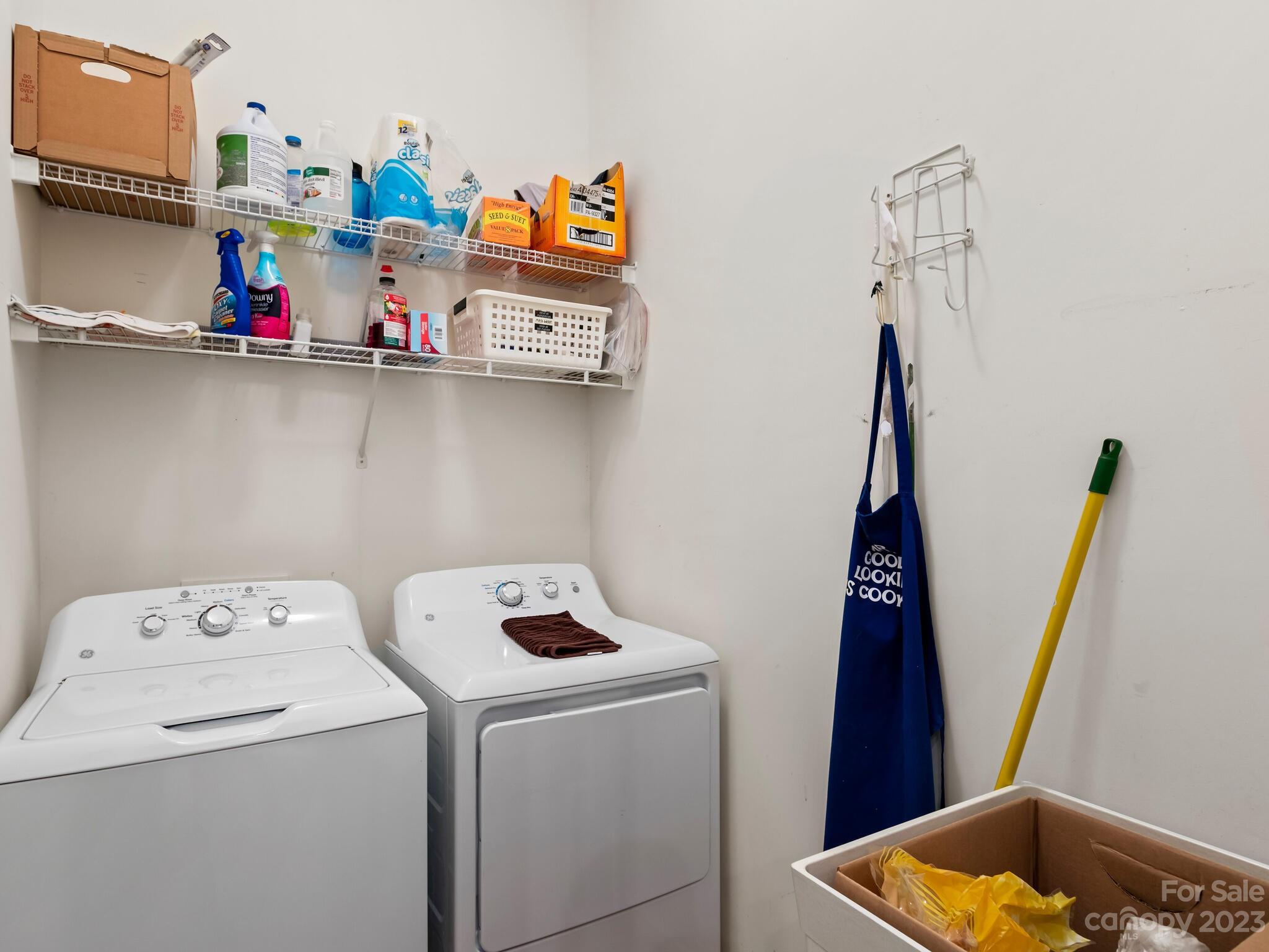 Laundry room with a washer and dryer beneath shelves of cleaning supplies.