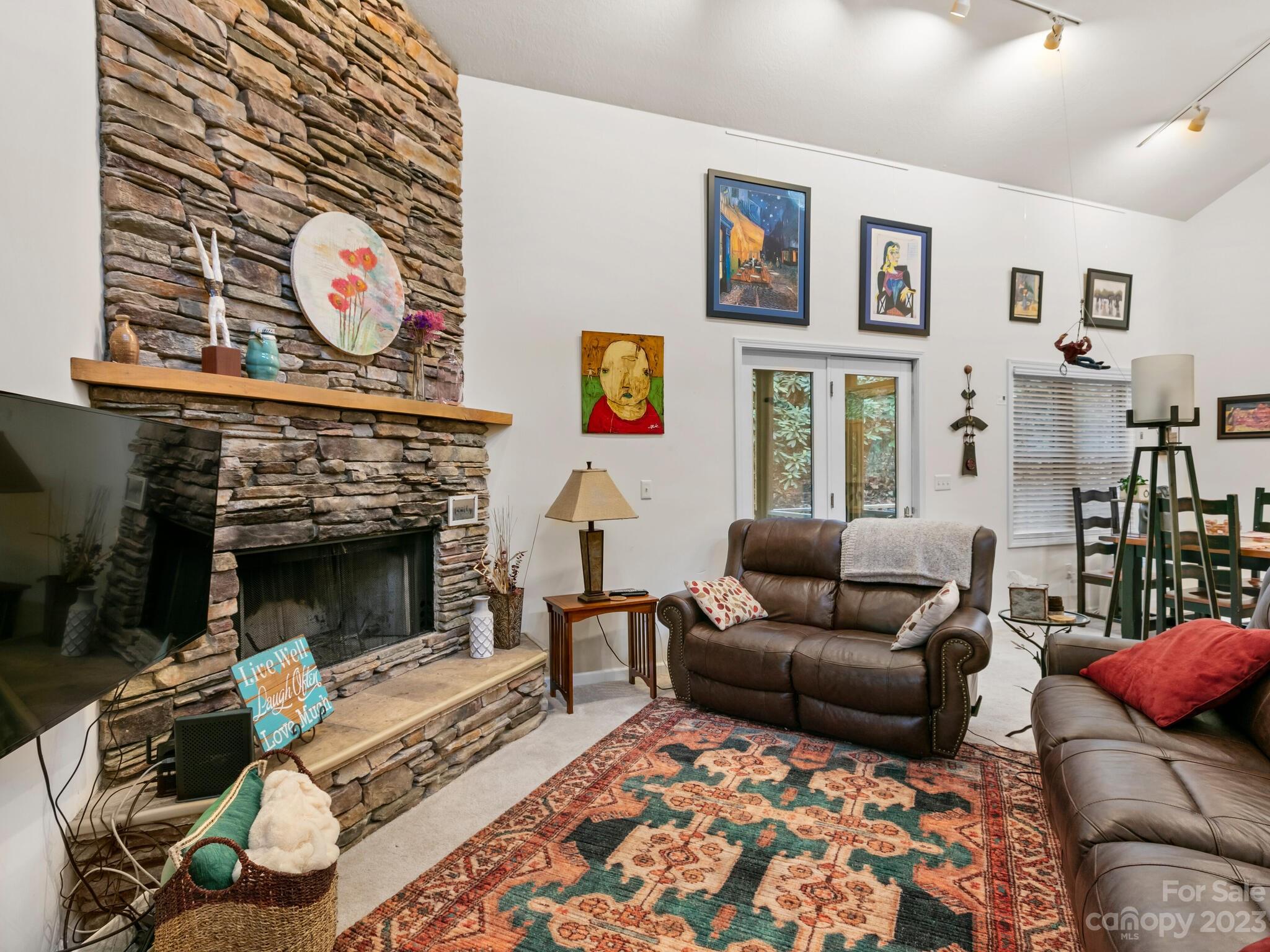 Living room with a tall stone fireplace, vaulted ceiling, leather sofas, and colorful patterned rug.