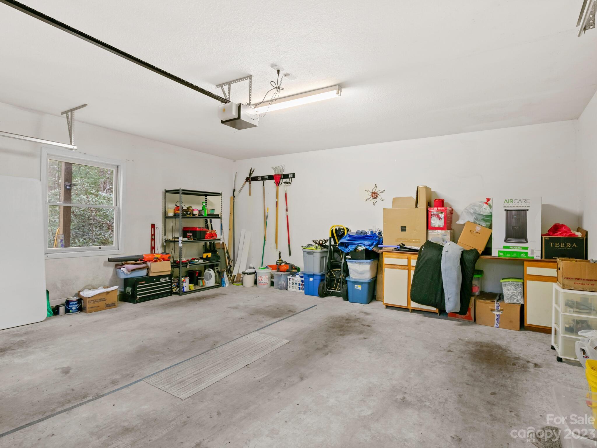 Garage with a concrete floor, window, tools, storage bins, and cabinets along the walls.