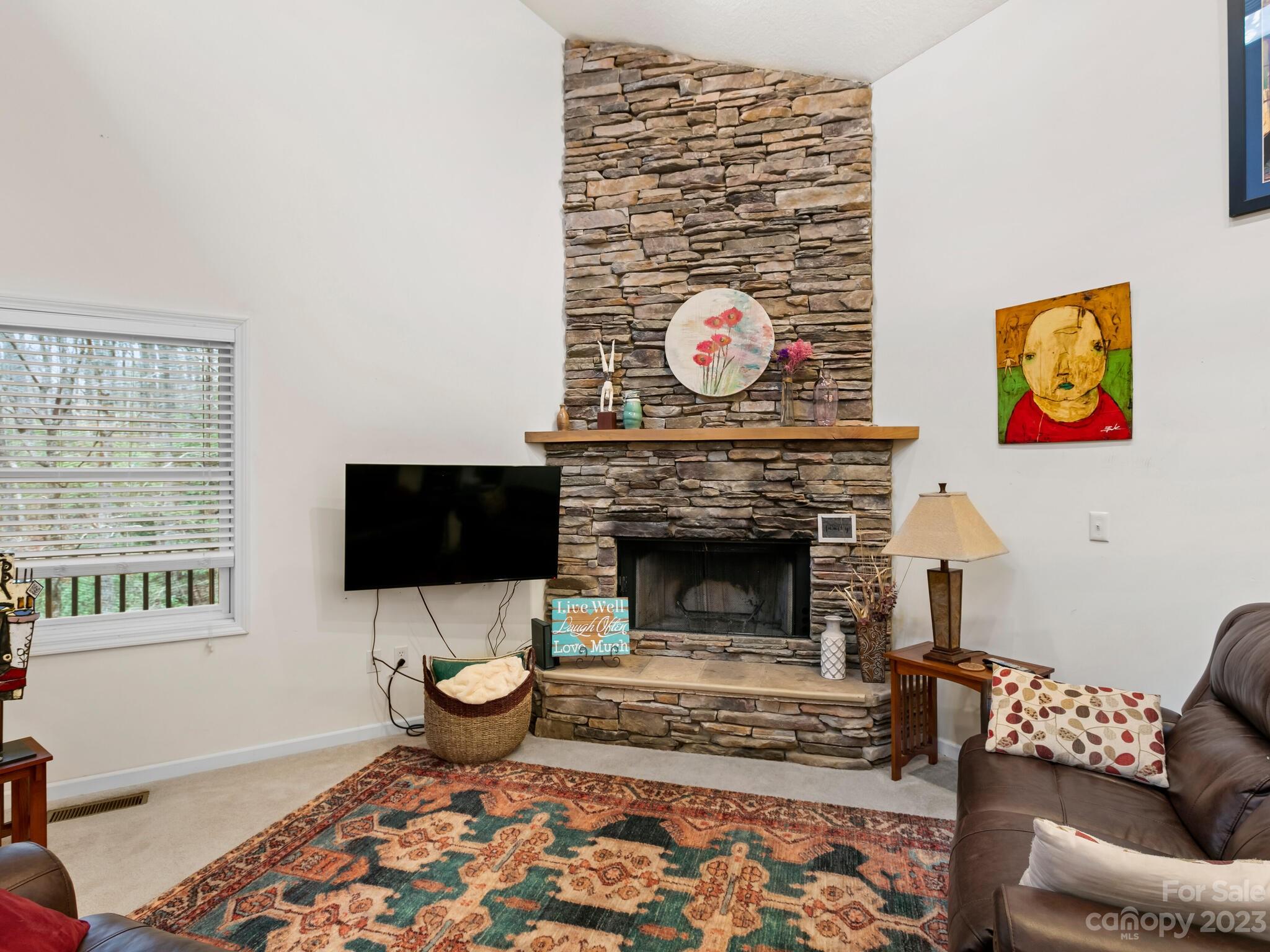 Living room with a tall stacked-stone fireplace, wall-mounted TV, patterned rug, and leather seating.