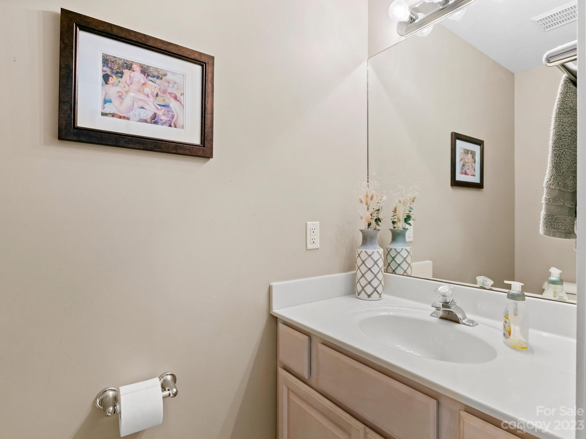 Bathroom vanity with a white sink, light wood cabinets, and a large mirror.
