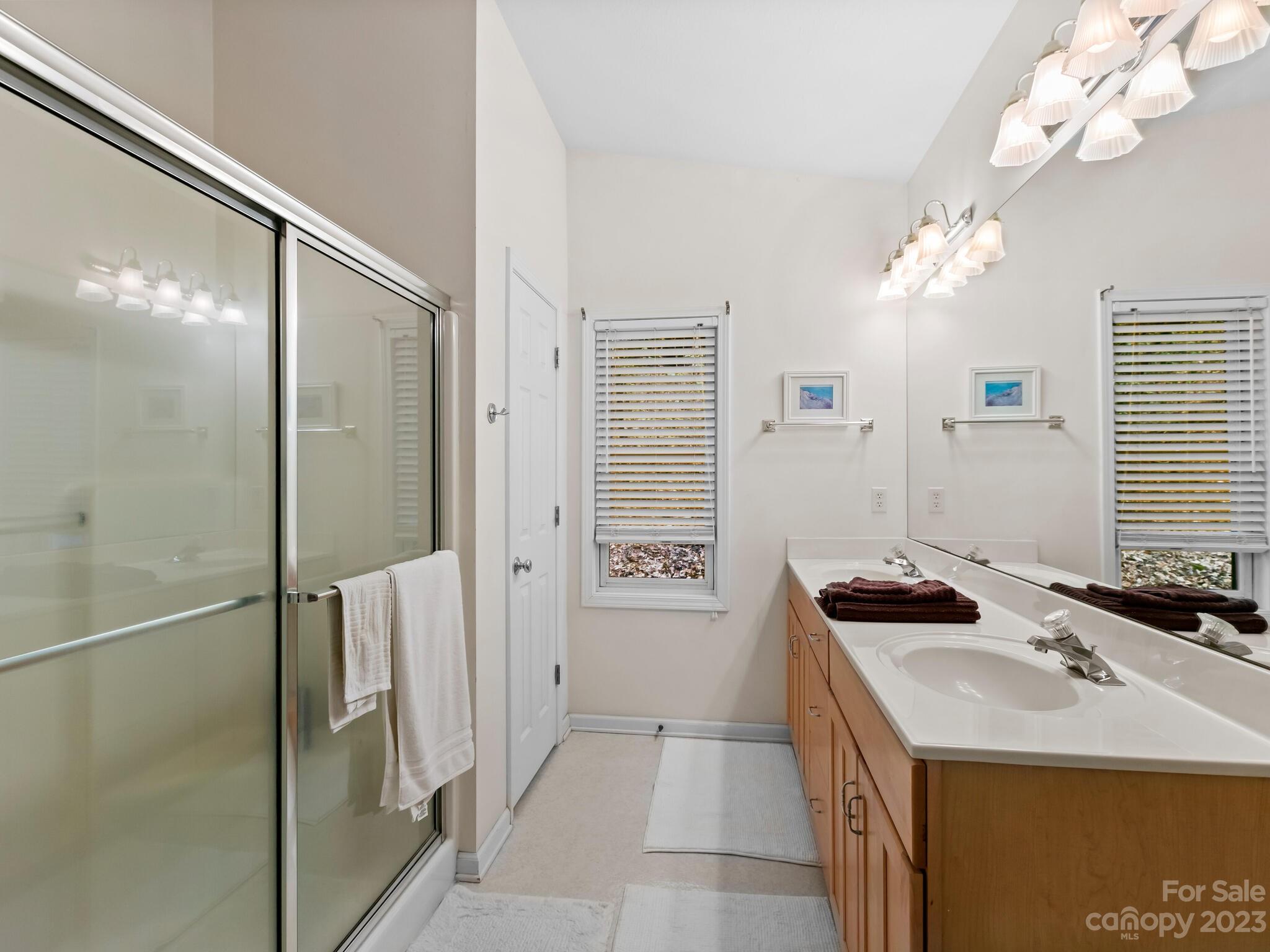 Bathroom with glass shower and long double-sink wood vanity beneath a large mirror.