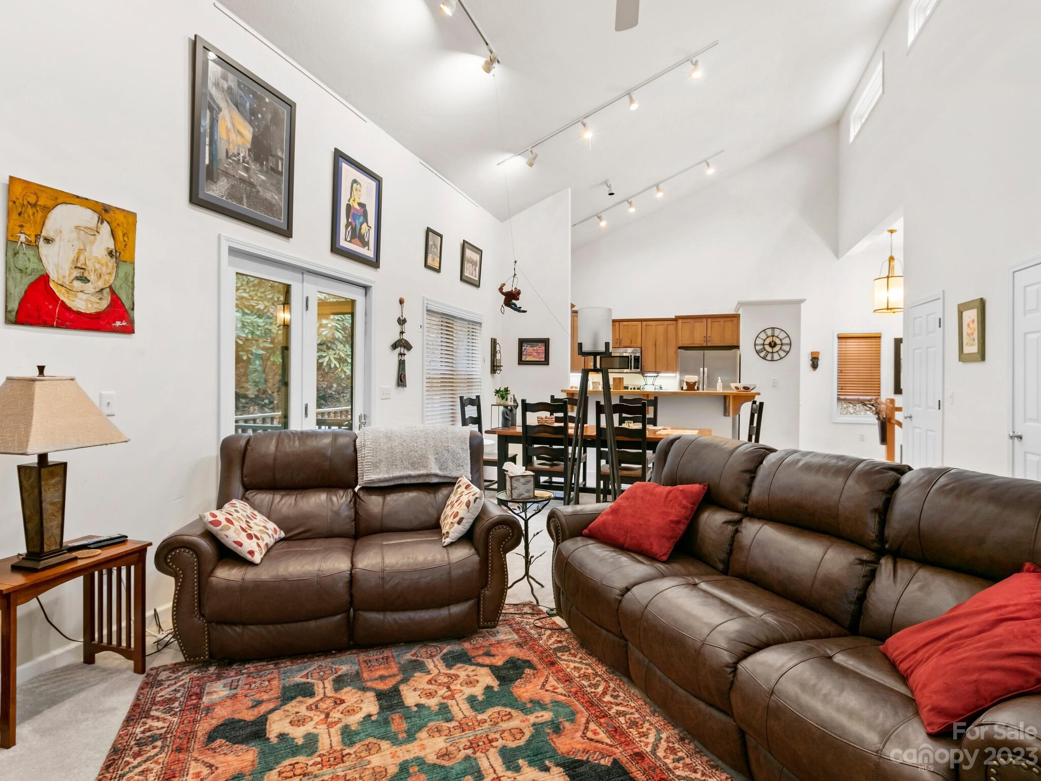 Furnished living room with vaulted ceiling, leather sofas, and an open kitchen-dining area.