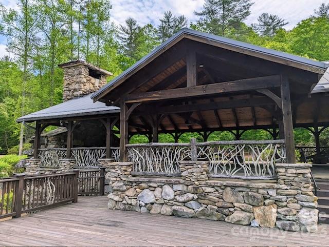 Covered timber pavilion with a stone chimney, rustic branch railings, and a broad wooden deck.