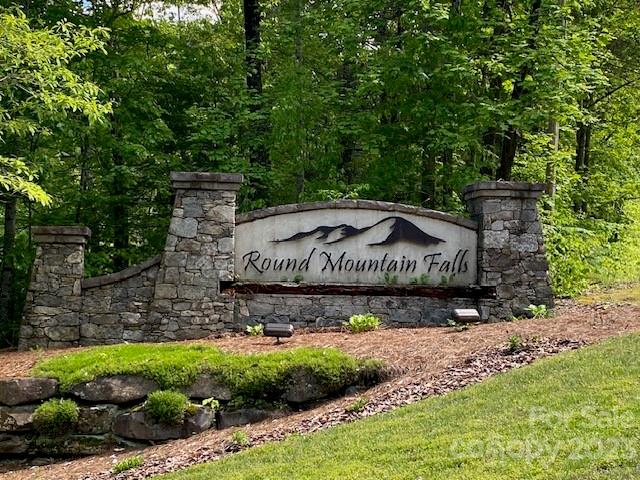 Round Mountain Falls entrance sign between stone pillars, surrounded by trees and landscaping.