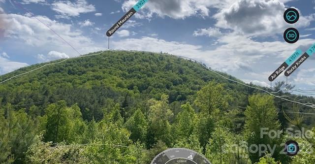 Wooded mountain ridge viewed from a property lot beneath a partly cloudy sky.