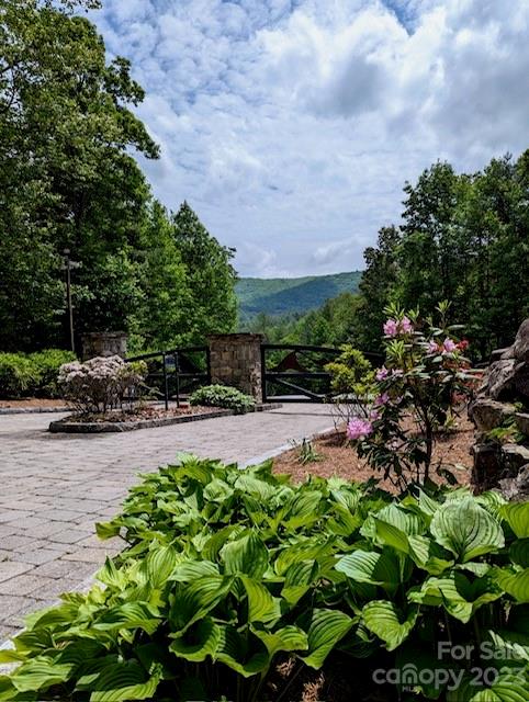 Land entrance with a stone-and-black gate, landscaped shrubs, and distant mountain views.