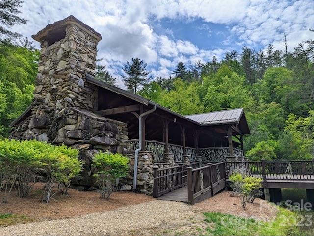 Stone fireplace and covered wooden pavilion with a raised deck amid dense greenery.