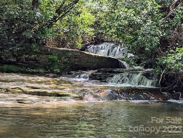 Waterfall flowing over rocky ledges into a wooded creek pool.