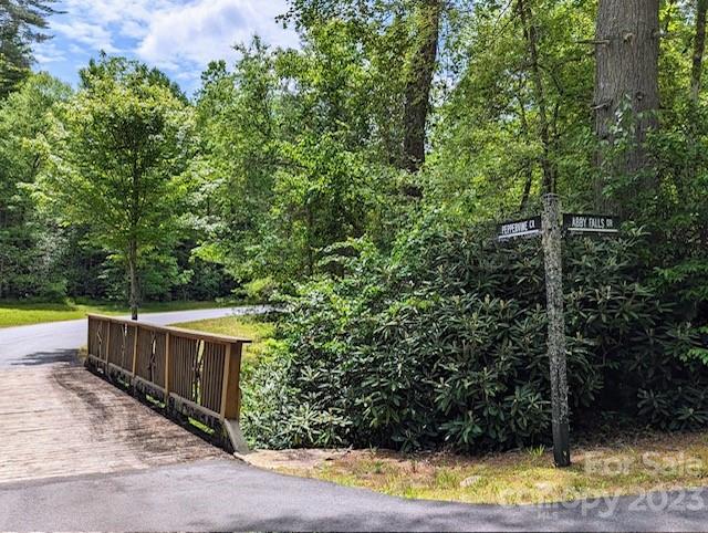 Wooded property entrance beside a paved road, marked by street signs and a wooden pedestrian bridge.