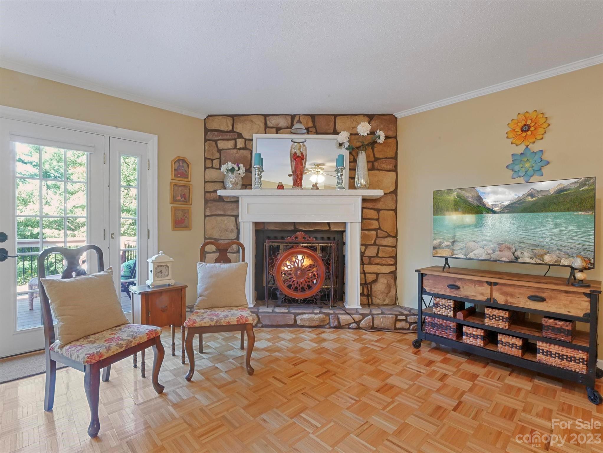 Living room with a stone fireplace, parquet floor, and French doors opening onto a deck.