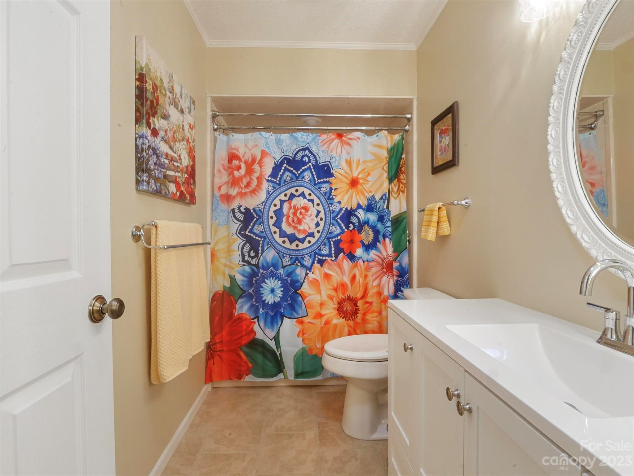 Bathroom with a floral shower curtain, white vanity, and ornate mirror.