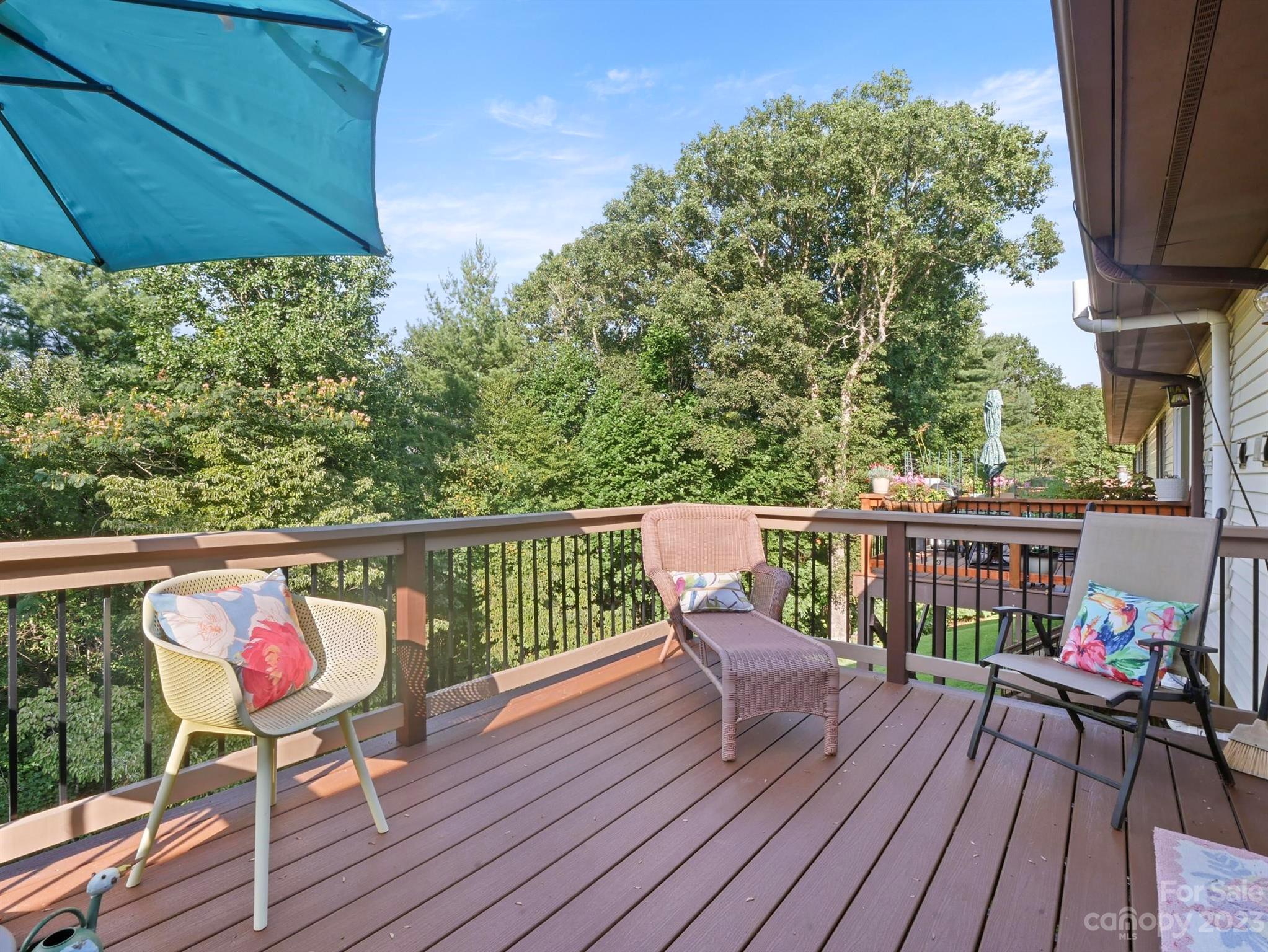 Furnished deck with patio seating and a blue umbrella overlooking a wooded yard.