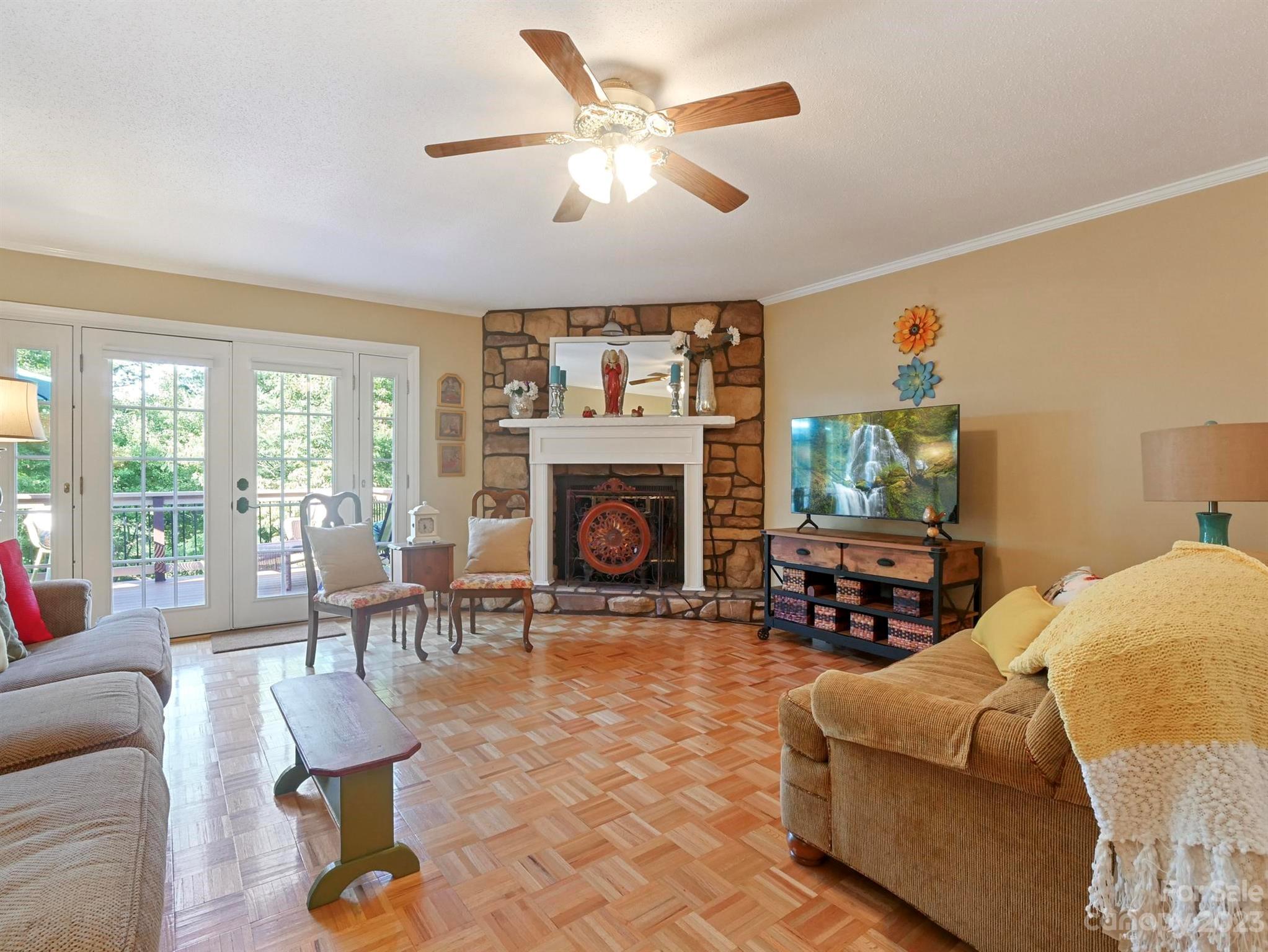 Living room with a stone fireplace, parquet floor, and French doors opening to a deck.