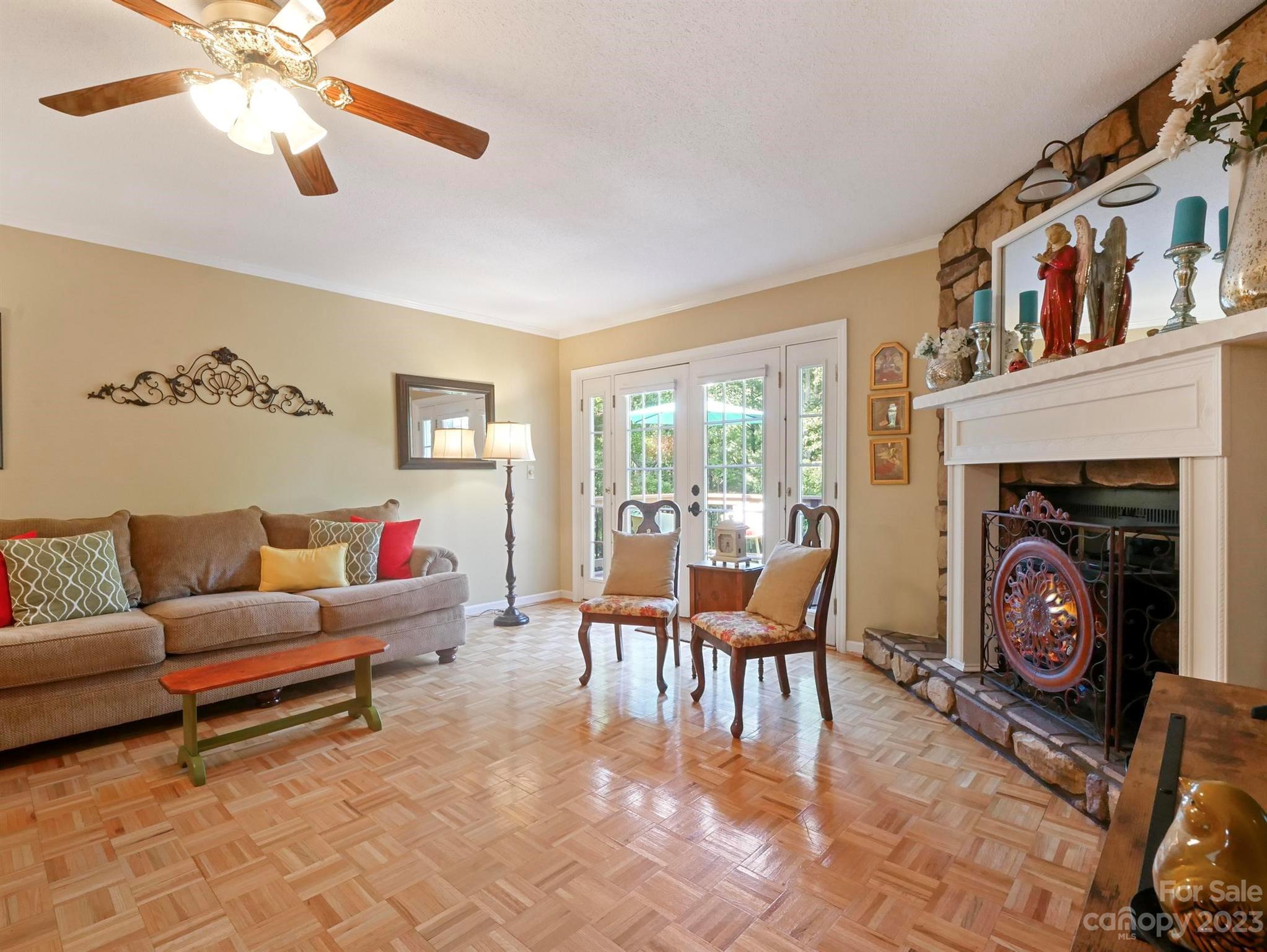 Living room with a stone fireplace, brown sofa, parquet floor, and French doors.
