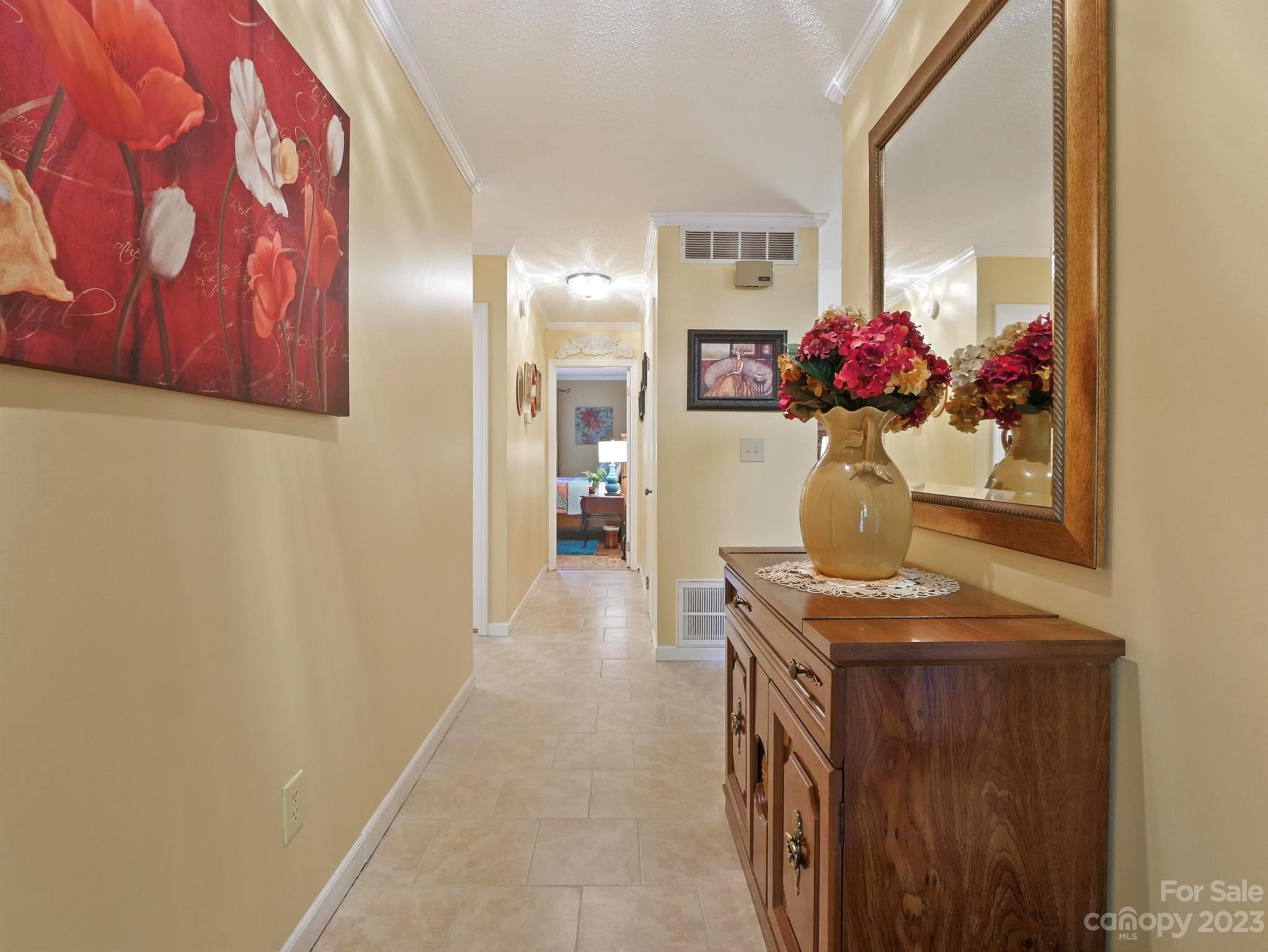 Tiled hallway with a wooden sideboard, red flowers, and a large wall mirror.