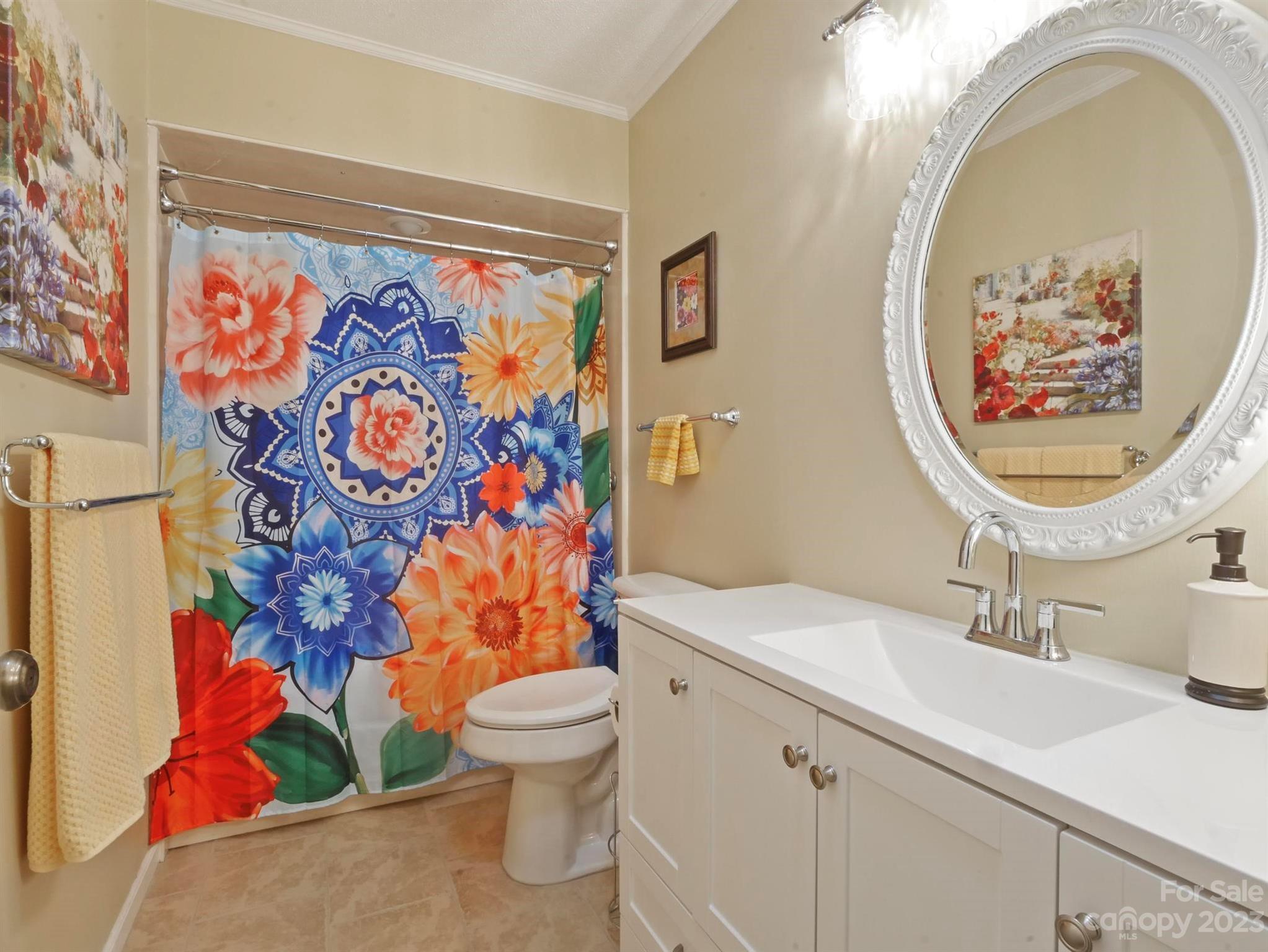 Bathroom with a white vanity and ornate oval mirror beside a vivid floral shower curtain.
