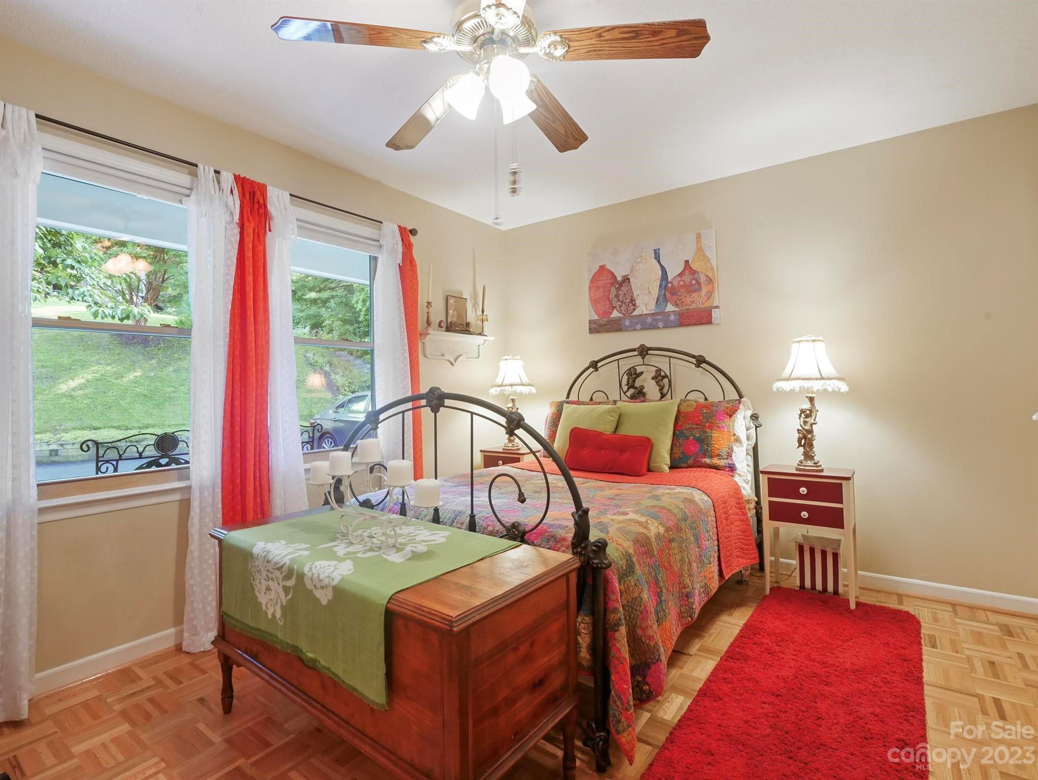 Furnished bedroom with colorful bedding, a wooden storage bench, and red-and-white curtains.