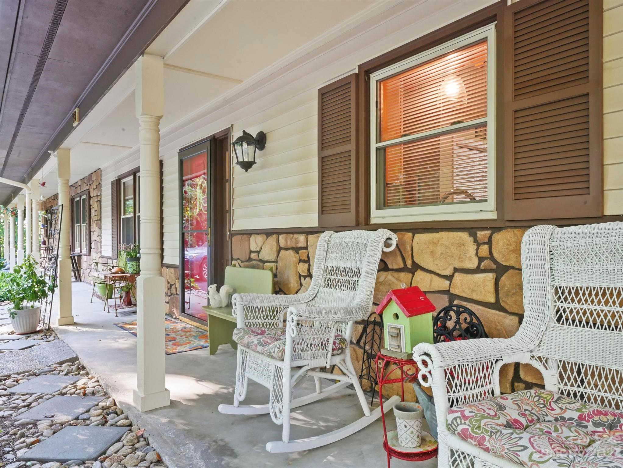 Covered front porch with white wicker rocking chairs, brown shutters, and a stone veneer wall.