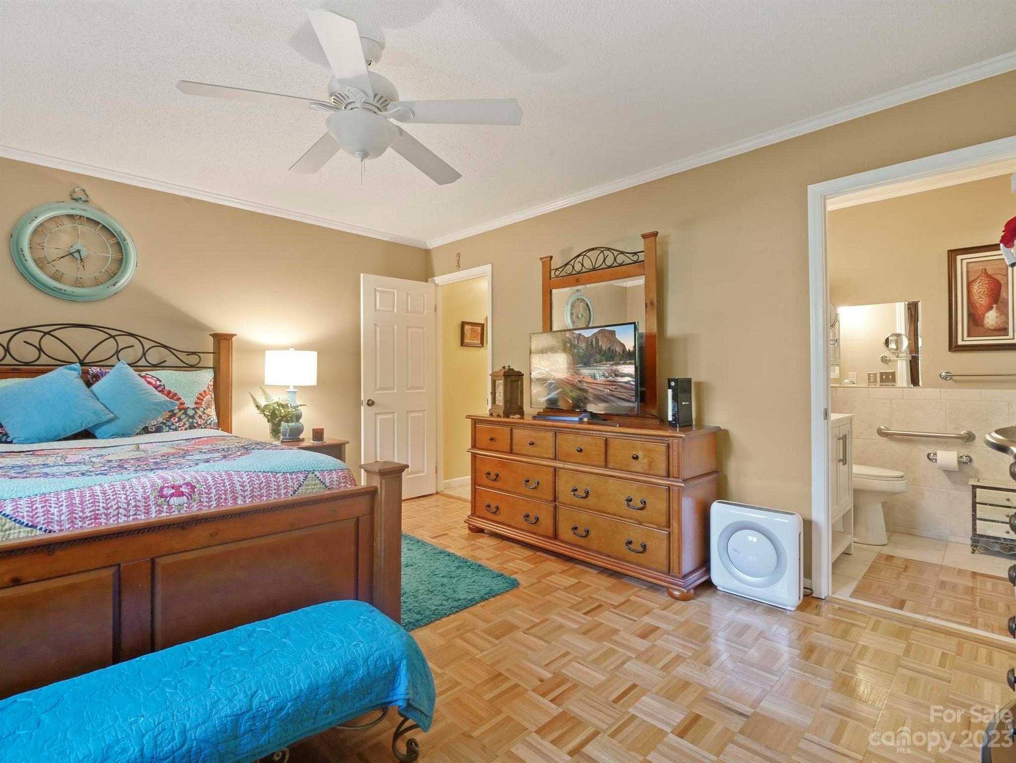 Furnished bedroom with colorful bedding, parquet flooring, and an open doorway to an accessible bathroom.