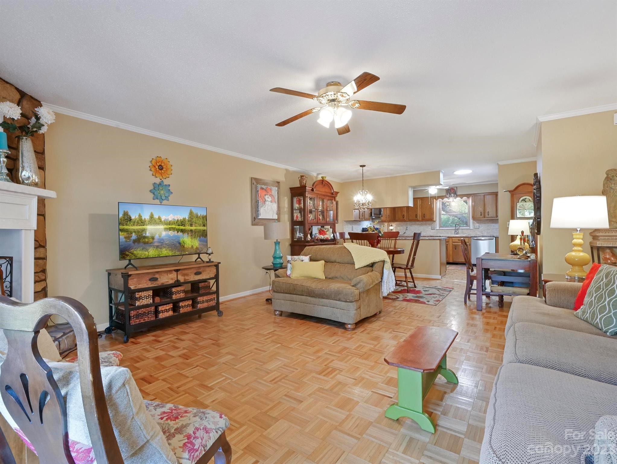 Open-plan living room with parquet floors, a stone fireplace, and the dining area and kitchen beyond.